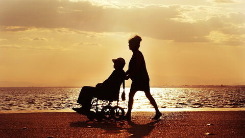 Ein Mann im Rollstuhl wird am Strand von einer Frau gefahren